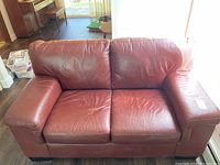 Front view of the red leather loveseat sofa showing texture, seat cushions, and armrests.