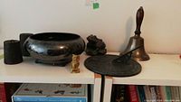 Overview photo showing the silver plate bowl, owl figurine, lead weights, brass bell, brass frog, and an additional decorative metal object with circular pattern.
