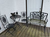 Full view of black metal garden set including two folding chairs, round bistro table with butterfly decoration, and garden bench showing weathering.