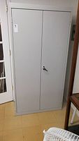 Front view of a closed tall gray metal storage cabinet with two doors and a metal lick handle.