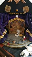 Front view of wooden Punch and Judy stage with purple velvet curtains and gold trim, illustrated backdrop and some props on stage floor