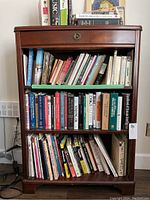 Front view of vintage wooden bookshelf with three shelves full of books and a drawer at the top.