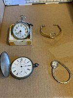 Overview of all four watches on a cardboard surface, showing two pocket watches and two ladies wristwatches.