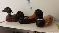 Photo showing three wooden duck decoys varying in color and size arranged on a white surface.