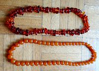 Two amber-colored necklaces laid flat on wooden surface, showing full length and bead shape. One necklace is darker and chunky, the other lighter and round beads.