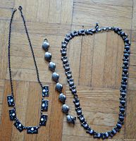 Photo showing all three items laid flat: two necklaces and one bracelet, highlighting overall style and design.