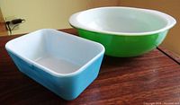 Green round Pyrex bowl with white interior and blue rectangular Pyrex dish on table.