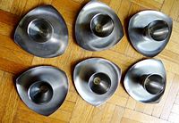 Overhead photo showing all six stainless steel egg holders arranged on wood floor, highlighting their brushed metal finish and triangular base design with rounded corners.