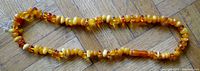 Top view showing the full length of the amber or bakelite bead necklace arranged on a wooden floor.