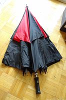 Closed umbrella showing black exterior with red parts and black handle on wooden floor.