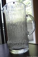 Full view of the clear textured glass jug showing the vertical ribbed pattern and bubble details, with handle and spout visible.