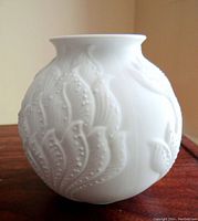 Front view of white porcelain vase showing raised floral embossed pattern and round shape.