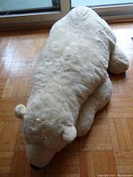 Overhead side view of large white stuffed polar bear plush toy on wooden floor.