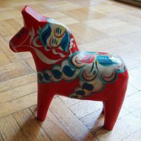 Side view of a red wooden Dala horse figurine with traditional painted decorations on its body and head.