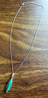 Full view of silver chain necklace laid flat on wooden surface, showing entire chain and pendant.