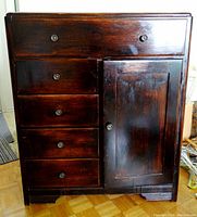 Front view of dark-stained solid wood cabinet showing five drawers and cupboard door with metal knobs.