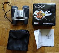 Binoculars displayed with original box, soft pouch, and instruction sheet on wood floor.