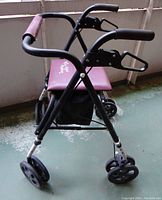 Side view showing maroon padded seat, black metal frame, and four black wheels. Hand brakes visible on handles.