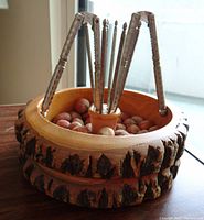 Wood bowl with bark edge filled with hazelnuts and eight nutcracker forks placed inside, showing the overall look and contents.