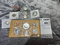 Full lot including sealed coin set, loose coins in protective sleeves, and plastic bags, laid out on grey fabric.