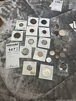 Photo of a wide variety of Canadian coins including antique, vintage, and contemporary varieties laid out on fabric. Some coins are in protective holders with noted years 1924, 1927, 1929, 1930, along with some loose coins. Includes note cards indicating coin details.
