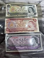Three Canadian paper currency bills showing front of $1 gray, $2 red, and $10 purple bill with Queen Elizabeth II present on all