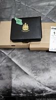 Closed black case with gold Canadian coat of arms logo and number '71' sticker, resting on cardboard box