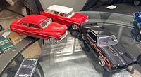 Three die cast metal model cars including black Pontiac GTO with flame decals and opening doors and hood, red coupe and red and white station wagon on glass table.