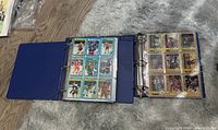 Two blue binders opened flat on carpet showing NHL hockey cards in plastic protective pages, each page containing 12 cards