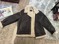 Full view of the men’s sheepskin coat showing the dark brown leather exterior, cream sheepskin lining, large collar, and sleeve cuffs.