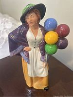 Front and slightly angled view of Royal Doulton Balloon Lady figurine on a dark wood surface.