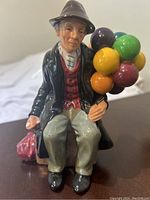 Front view showing seated elderly man holding colorful balloons and red bag beside him.