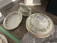 Gravy boat on two underplates, stack of underplates, stack of round bowls, two lids atop plates