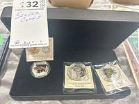 Overview of three coins in black presentation case, two in sealed packaging