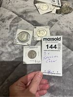 Photo showing three special coins including two Kennedy half dollars and one quarter with counterstamp with prices noted ($80, $80, $30) and label showing lot number 144.