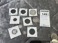 Collection of United States coins including various one cent coins, a 1937 half dollar, and silver dollars from the late 19th and early 20th century. Coins in protective holders with dated labels and pricing.