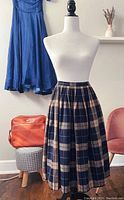 Front view of the vintage pleated wool skirt on a mannequin showing the navy and beige plaid pattern with pleats and medium length.