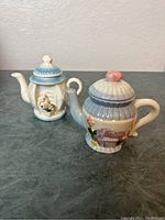Both vintage tiny teapots shown together on a surface with plain wall background