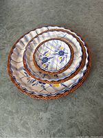 Three round ceramic tart/quiche baking dishes stacked inside each other, showing scalloped edges, floral pattern, and wicker lattice edging with some damage.