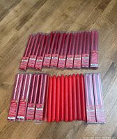 Multiple sets of red taper candles on wooden floor, some in packaging, some loose.