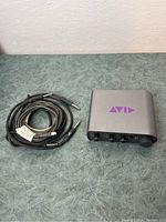 Avid Mbox Mini 3 interface alongside bundled audio cables with 1/4 inch connectors on green surface.