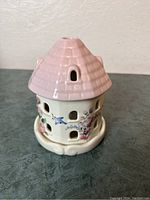 Ceramic candle holder shaped like a house with pink roof, decorated with blue birds and pink flowers, showing front and side details with window cutouts.