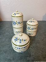 Whole set of three vintage Italian ceramic canisters shown with lids on top, decorated with blue flowers and green trim.