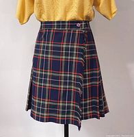 Front view of a vintage pleated plaid tartan skirt on a mannequin, showing the button detail at the waistband and the pleated pattern.