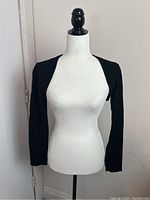 Full front view of black shoulder cover on a white dress form, showing fitted long sleeves and open front design.
