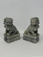 Front view of two grey soapstone Foo Dog statues seated on rectangular bases.