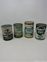 Front view of four vintage Quaker State oil cans showing original sealed tops and front labels including Quaker Maid Outboard Marine Motor Oil and three Quaker State Motor Oil cans.