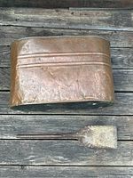 Top view of antique copper boiler and ash shovel on wooden surface showing copper boiler's size and patina and ash shovel's blade and handle.