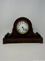 Front view of the wooden mantle clock with rounded top and brass feet