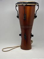 Front view of wooden hour-glass Batá drum with one large drumhead and tuning hardware visible.